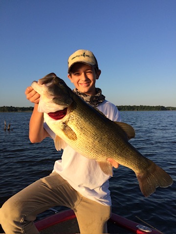 Young angler holding a huge largemouth bass on a boat